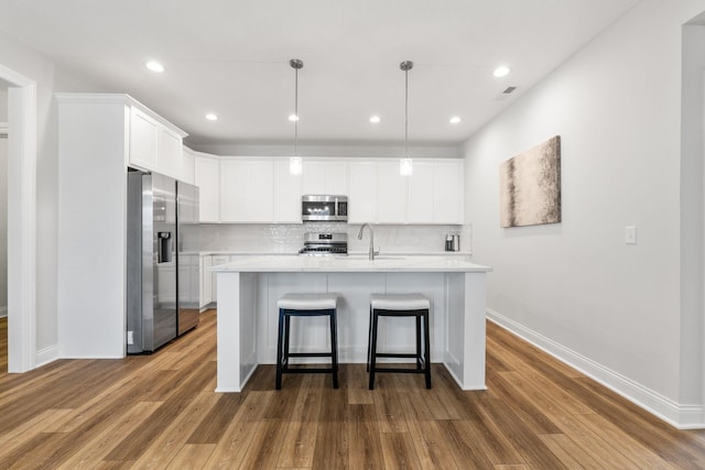 kitchen with appliances with stainless steel finishes, hardwood / wood-style flooring, pendant lighting, and an island with sink