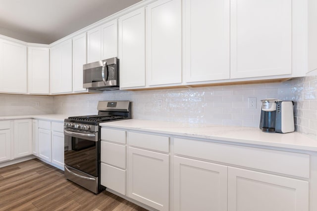 kitchen with white cabinetry, stainless steel appliances, light stone counters, backsplash, and hardwood / wood-style floors