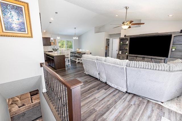 living room with ceiling fan with notable chandelier, dark hardwood / wood-style flooring, and vaulted ceiling