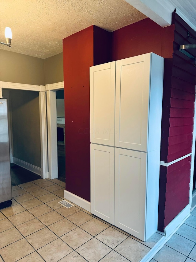 kitchen with a textured ceiling, white cabinetry, stainless steel refrigerator, and light tile patterned flooring