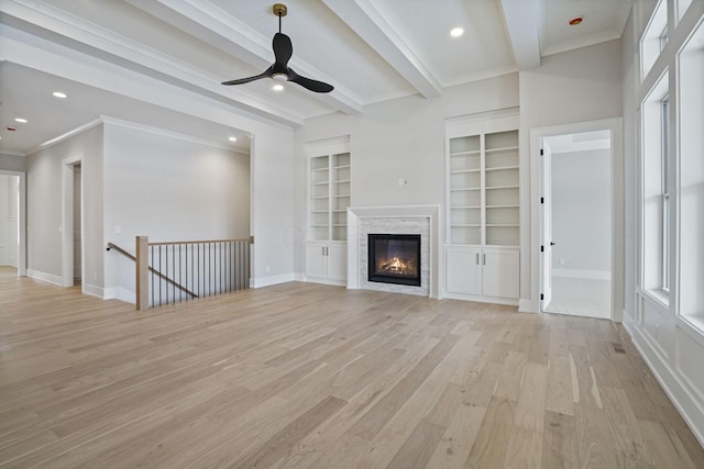 unfurnished living room featuring light hardwood / wood-style flooring, crown molding, built in features, beamed ceiling, and a stone fireplace