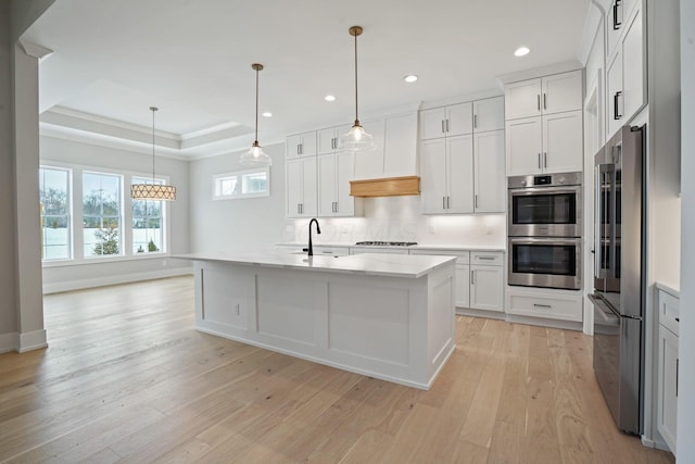 kitchen with a center island with sink, stainless steel appliances, hanging light fixtures, a tray ceiling, and white cabinets