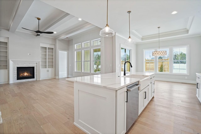 kitchen with dishwasher, an island with sink, light stone counters, white cabinetry, and built in features