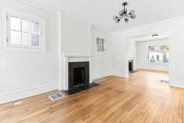 unfurnished living room featuring a tile fireplace, light wood-type flooring, a chandelier, and crown molding