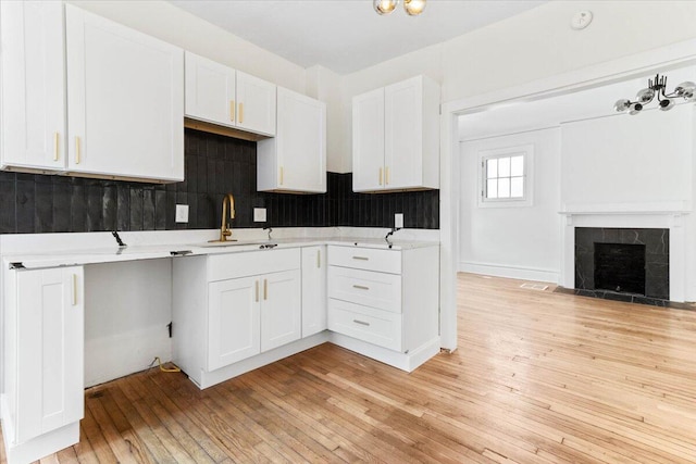 kitchen featuring decorative backsplash, a fireplace, sink, white cabinets, and light hardwood / wood-style floors