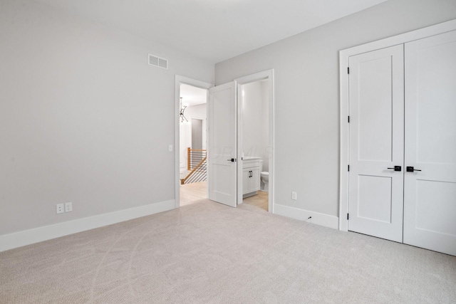 unfurnished bedroom with ensuite bathroom, a closet, and light carpet