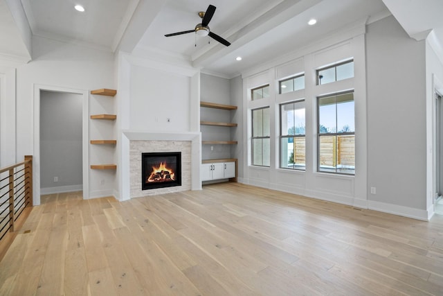 unfurnished living room featuring built in features, ceiling fan, ornamental molding, and a stone fireplace