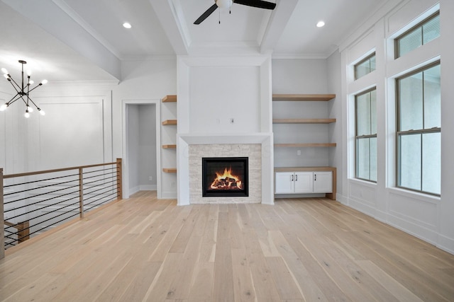 unfurnished living room with built in shelves, a stone fireplace, ornamental molding, and light hardwood / wood-style flooring