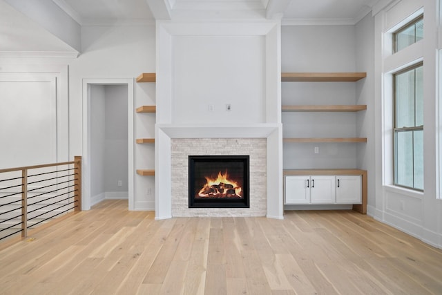 unfurnished living room with built in shelves, crown molding, a fireplace, and light hardwood / wood-style flooring