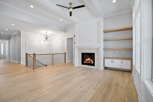 unfurnished living room with a stone fireplace, built in features, beamed ceiling, ceiling fan with notable chandelier, and light wood-type flooring