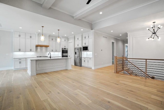 kitchen featuring appliances with stainless steel finishes, backsplash, a kitchen island with sink, pendant lighting, and white cabinetry