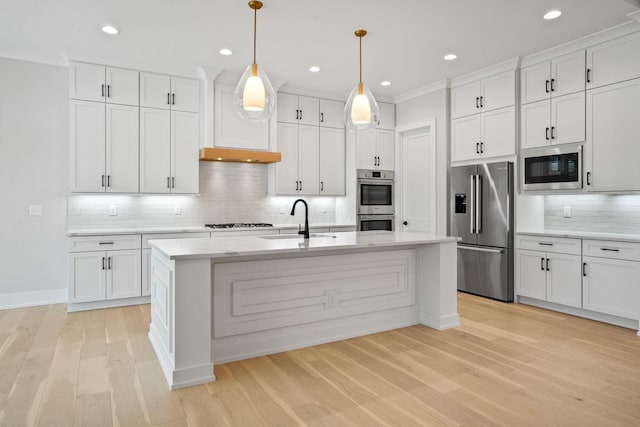 kitchen featuring white cabinetry, sink, hanging light fixtures, stainless steel appliances, and a kitchen island with sink