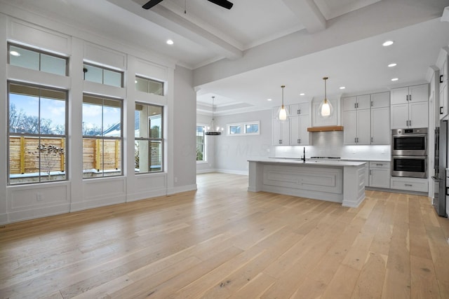 kitchen with stainless steel double oven, beam ceiling, a center island with sink, white cabinets, and hanging light fixtures