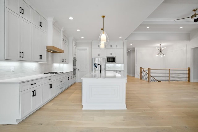 kitchen featuring white cabinetry, backsplash, built in appliances, decorative light fixtures, and a kitchen island with sink