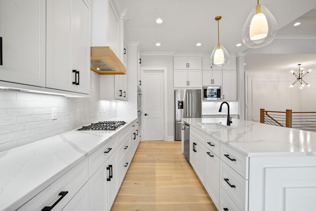 kitchen with appliances with stainless steel finishes, a kitchen island with sink, sink, white cabinets, and hanging light fixtures