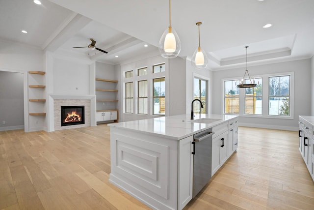 kitchen featuring dishwasher, white cabinets, sink, built in shelves, and an island with sink