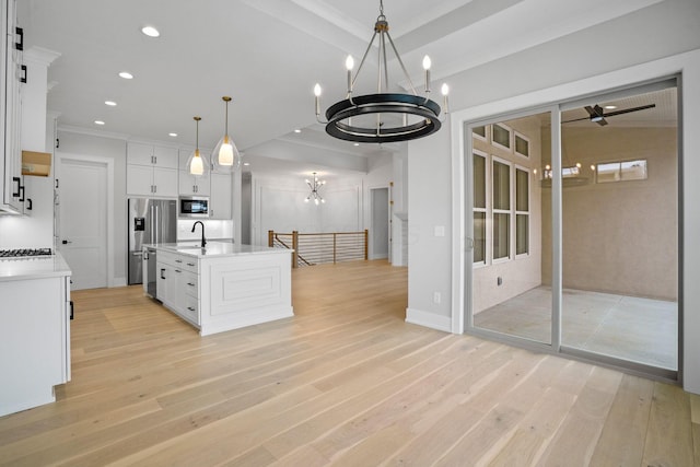 kitchen featuring sink, stainless steel appliances, an island with sink, decorative light fixtures, and white cabinets