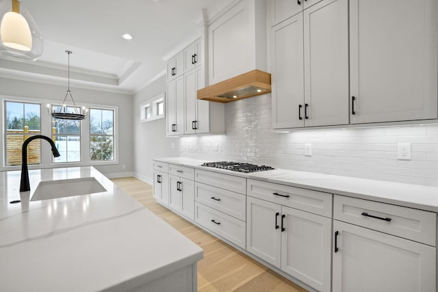 kitchen with white cabinetry, sink, hanging light fixtures, stainless steel gas stovetop, and custom exhaust hood