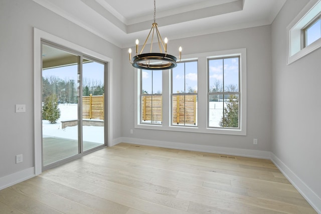 unfurnished dining area featuring a raised ceiling, light hardwood / wood-style floors, ornamental molding, and a notable chandelier