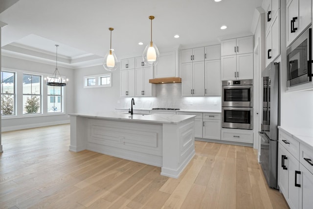 kitchen featuring a center island with sink, stainless steel appliances, sink, and a tray ceiling