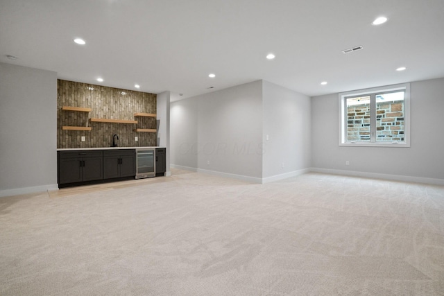 unfurnished living room with bar area, light colored carpet, wine cooler, and wood walls