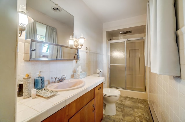 bathroom featuring vanity, toilet, a shower with shower door, and tile walls