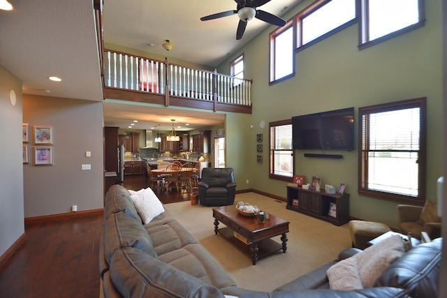 living room with ceiling fan with notable chandelier, a towering ceiling, hardwood / wood-style flooring, and plenty of natural light