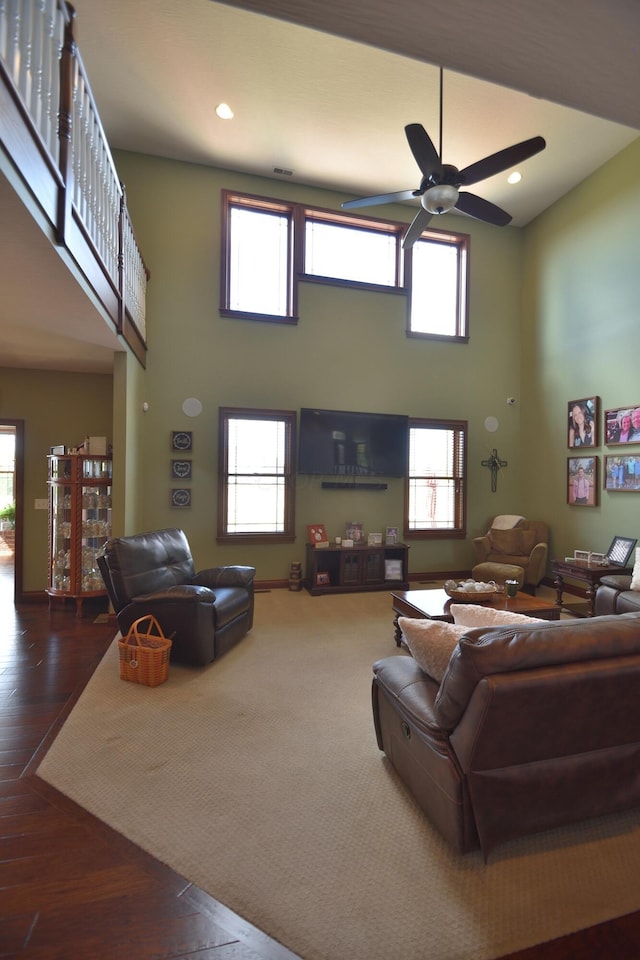 living room with a towering ceiling, dark hardwood / wood-style floors, plenty of natural light, and ceiling fan