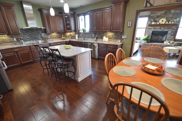 kitchen with dishwasher, wall chimney exhaust hood, decorative backsplash, decorative light fixtures, and a kitchen island