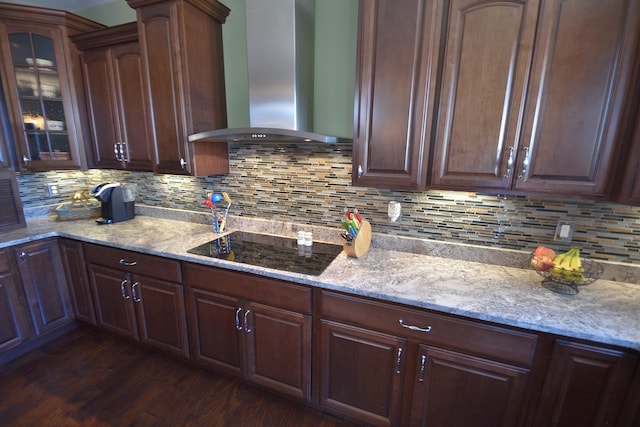 kitchen featuring wall chimney exhaust hood, decorative backsplash, black electric cooktop, light stone counters, and dark hardwood / wood-style flooring