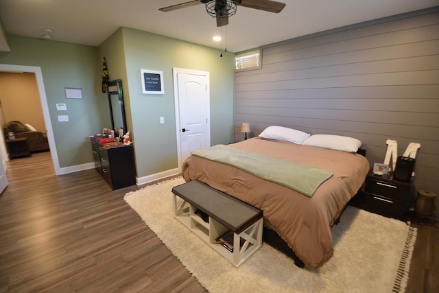 bedroom with hardwood / wood-style flooring, ceiling fan, and wood walls