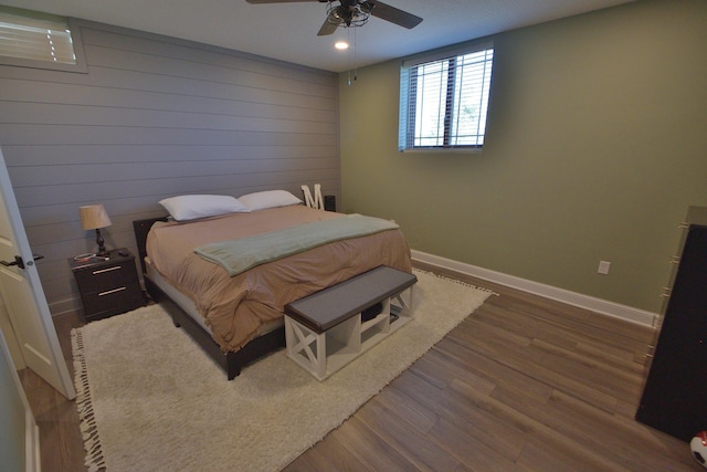 bedroom with hardwood / wood-style flooring, ceiling fan, and wooden walls