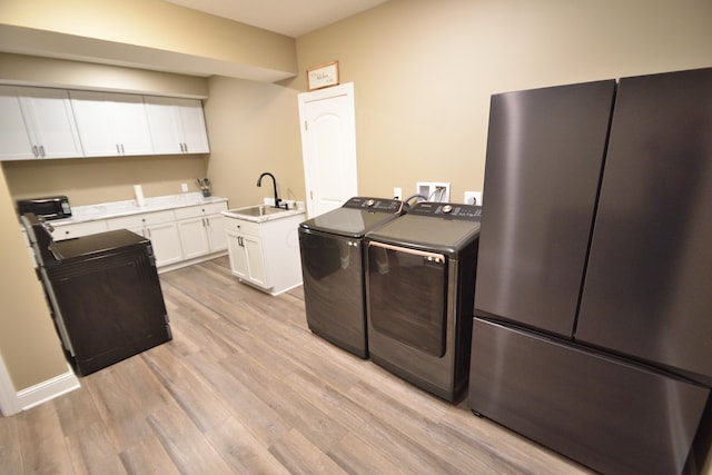 kitchen featuring washing machine and clothes dryer, sink, white cabinets, and light hardwood / wood-style floors