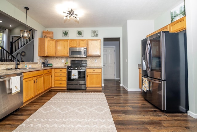 kitchen with appliances with stainless steel finishes, decorative light fixtures, dark wood-type flooring, and sink