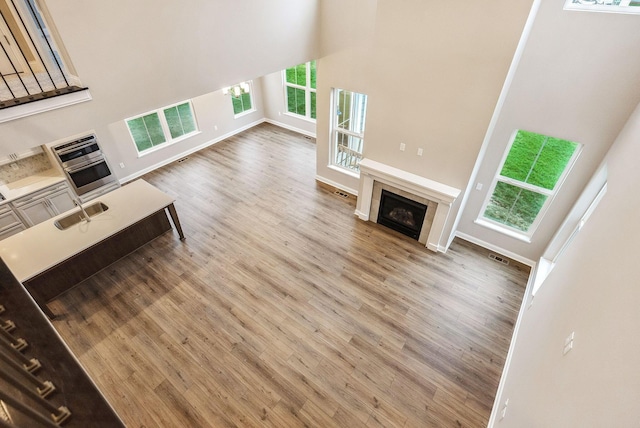 unfurnished living room with a tile fireplace, wood-type flooring, a towering ceiling, and sink