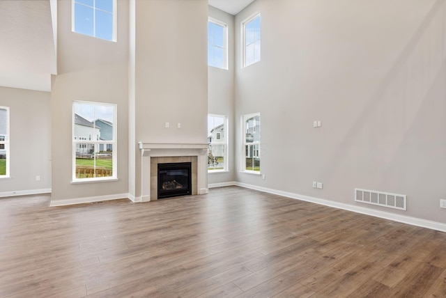 unfurnished living room with plenty of natural light, wood-type flooring, a towering ceiling, and a tiled fireplace