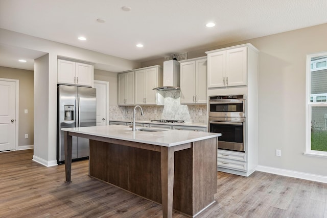 kitchen featuring sink, wall chimney exhaust hood, light hardwood / wood-style floors, white cabinets, and appliances with stainless steel finishes