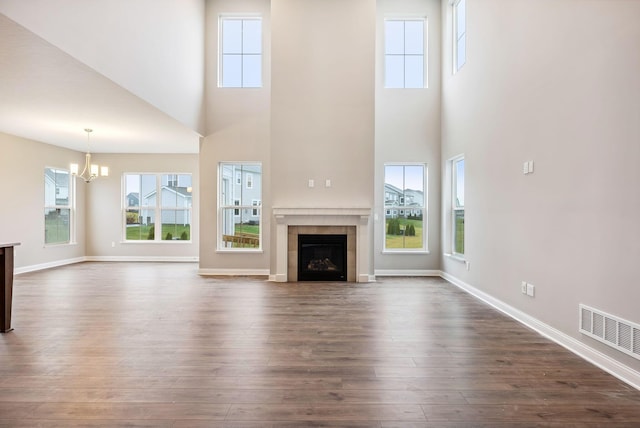 unfurnished living room with a fireplace, a towering ceiling, dark wood-type flooring, and a notable chandelier