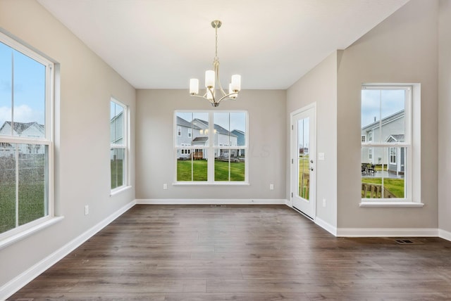 unfurnished dining area with dark hardwood / wood-style floors, a healthy amount of sunlight, and an inviting chandelier