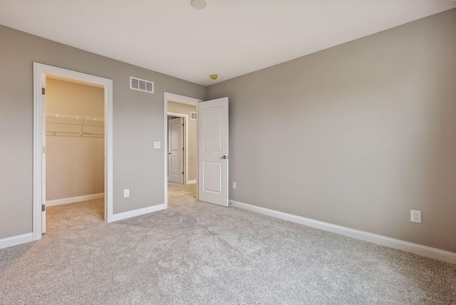 unfurnished bedroom with a walk in closet, light colored carpet, and a closet