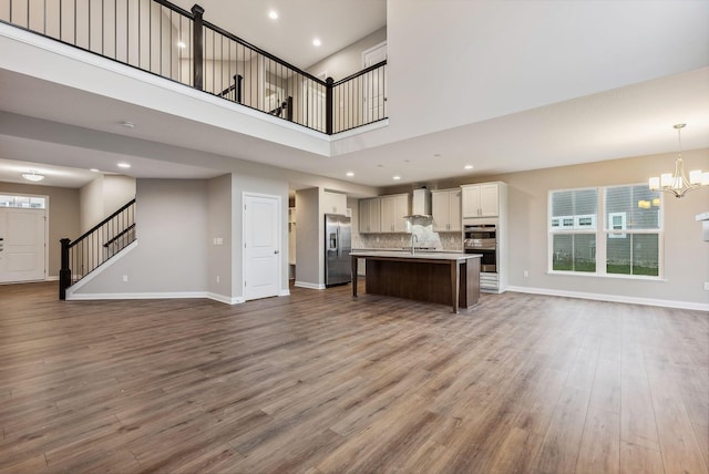 unfurnished living room featuring a chandelier, wood-type flooring, a towering ceiling, and sink