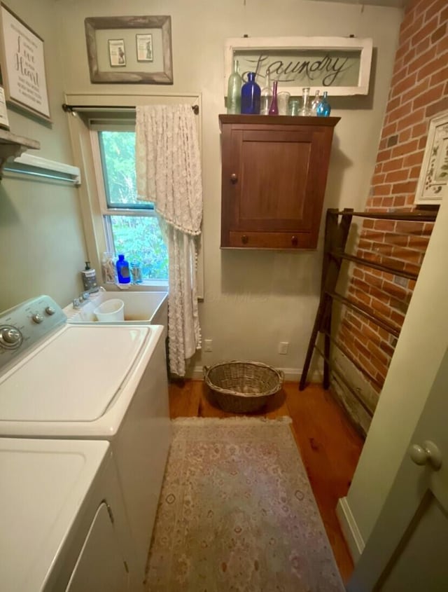 laundry room featuring hardwood / wood-style floors, sink, brick wall, and washing machine and clothes dryer