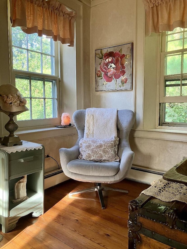 living area featuring hardwood / wood-style flooring, baseboard heating, and plenty of natural light