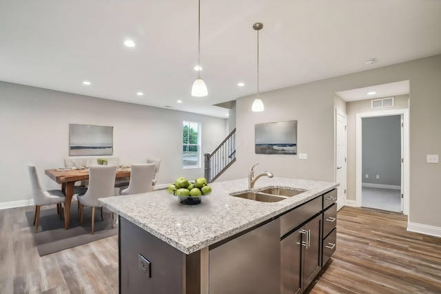 kitchen featuring hanging light fixtures, light hardwood / wood-style floors, sink, and a kitchen island with sink