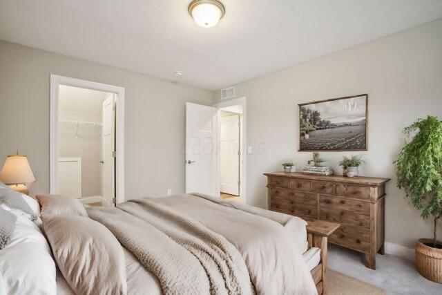 bedroom featuring a walk in closet, light colored carpet, and a closet