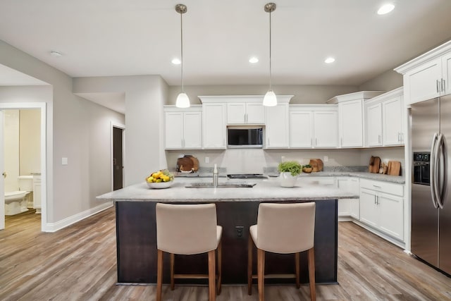 kitchen featuring white cabinets, stainless steel appliances, hanging light fixtures, and a center island with sink