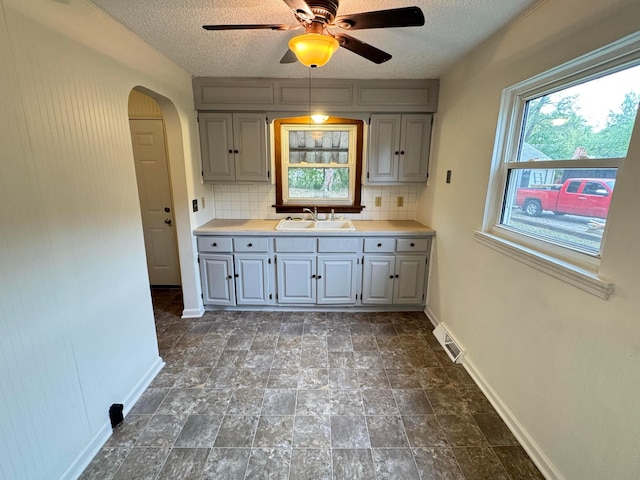 kitchen featuring gray cabinetry, sink, decorative backsplash, ceiling fan, and a textured ceiling