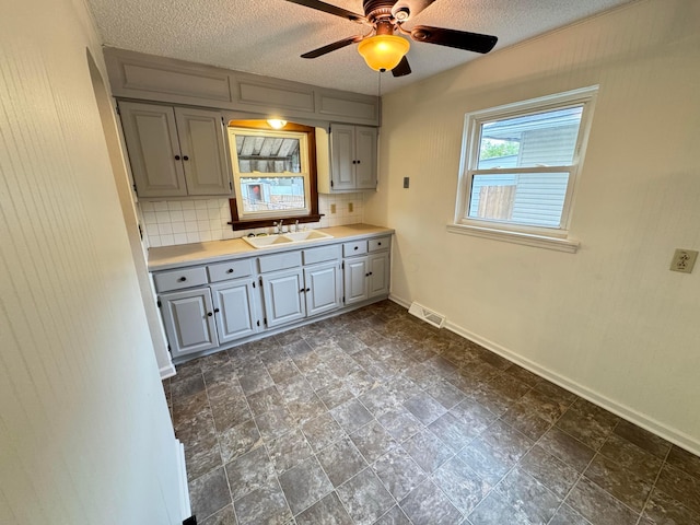 kitchen with gray cabinetry, ceiling fan, sink, tasteful backsplash, and a textured ceiling