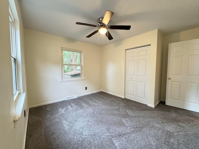 unfurnished bedroom with ceiling fan, dark carpet, a textured ceiling, and a closet