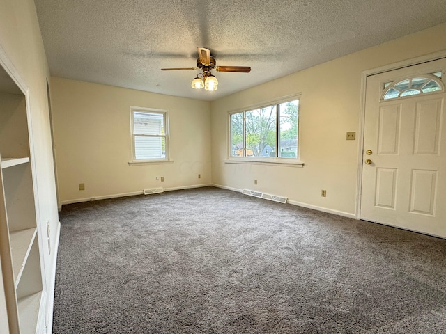 interior space featuring plenty of natural light, dark carpet, and ceiling fan